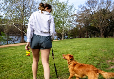 A woman walking with a dog in a park, holding a jar of CON-CRET creatine gummies, symbolizing a healthy lifestyle for better mental health.