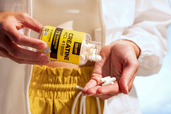Woman pouring a bottle of CON-CRĒT Creatine HCl capsules into her hand. 