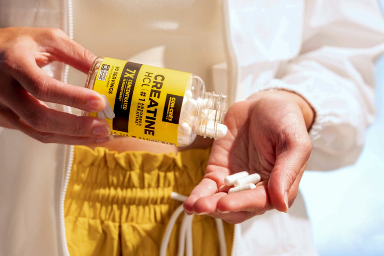 Woman pouring a bottle of CON-CRĒT Creatine HCl capsules into her hand. 