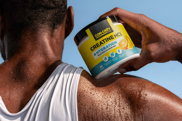 A close-up lifestyle shot of a man holding a tub of CON-CRĒT Creatine HCl Hydration supplement against his sweaty back and neck, with a clear blue sky in the background.